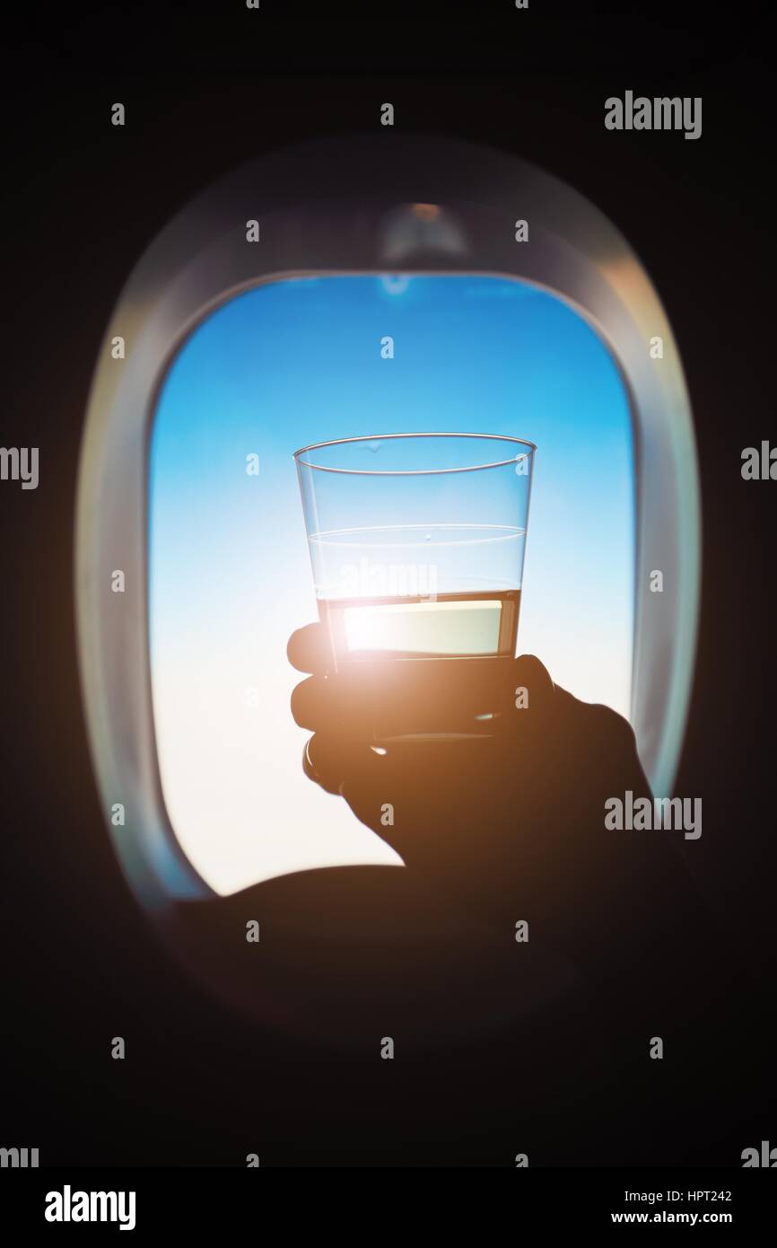 Comfortable traveling by airplane. Passenger is holding glass of the wine during the flight. Stock Photo