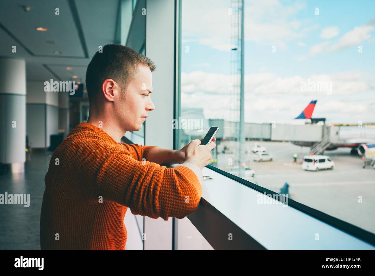 Young man with mobile phone waiting for a delayed flight inside airport terminal. Stock Photo