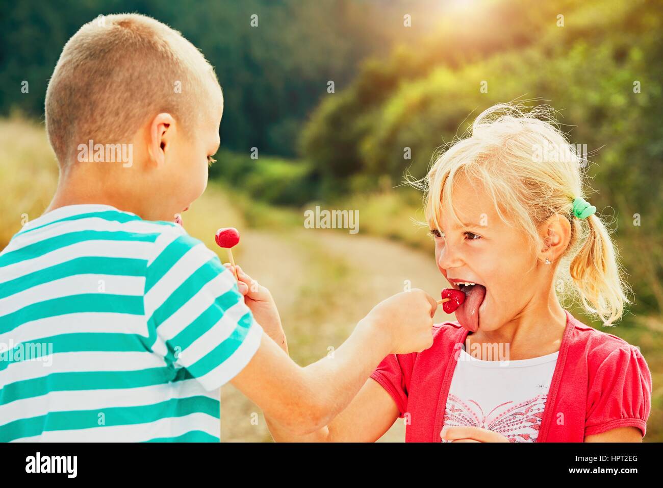 Children enjoying sunny day in holiday. Cheerful little boy and little girl tasting lollipops. Stock Photo