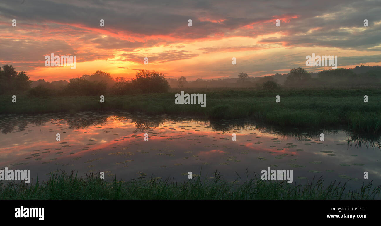 Foggy morning landscape on small lake with orange sky Stock Photo