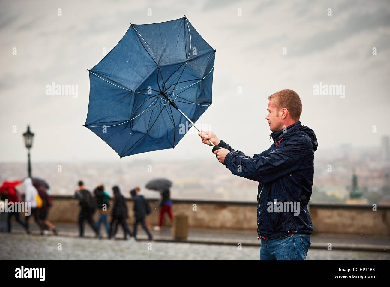 Rain in the city. Young man is holding blue umbrella during thunderstorm. Street of Prague, Czech Republic. Stock Photo