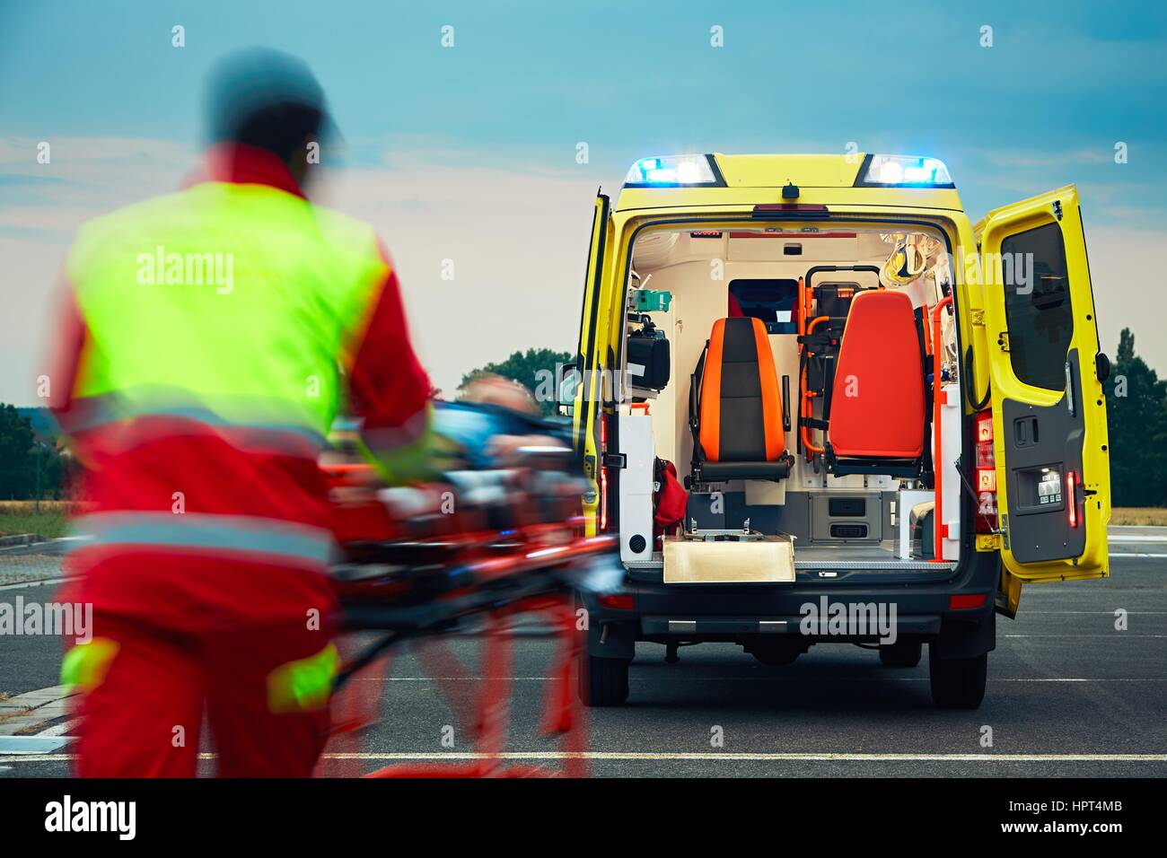 Emergency medical service. Paramedic is pulling stretcher with patient to the ambulance car. Stock Photo