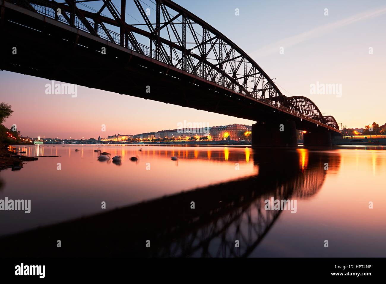 Amazing sunrise in the city. Railway bridge (with reflection in the river) and embankment in Prague, Czech Republic. Stock Photo