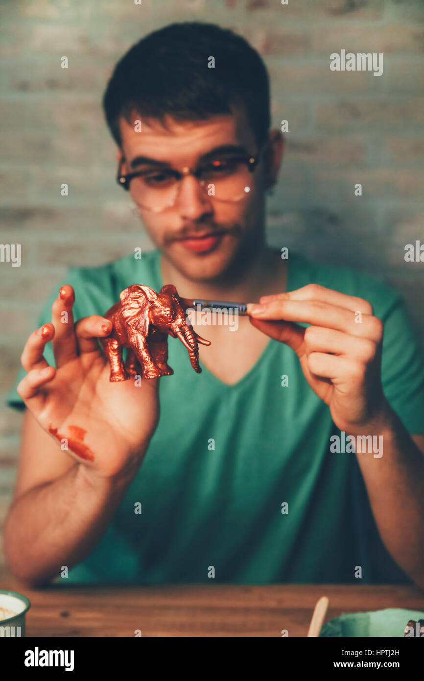 Young man painting plastic elephant figure with copper paint Stock Photo