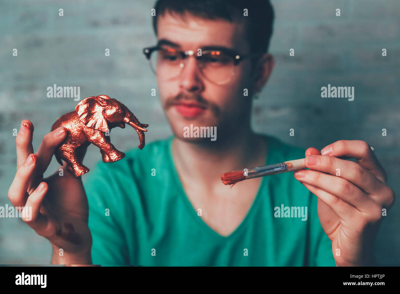 Young man painting plastic elephant figure with copper paint Stock Photo