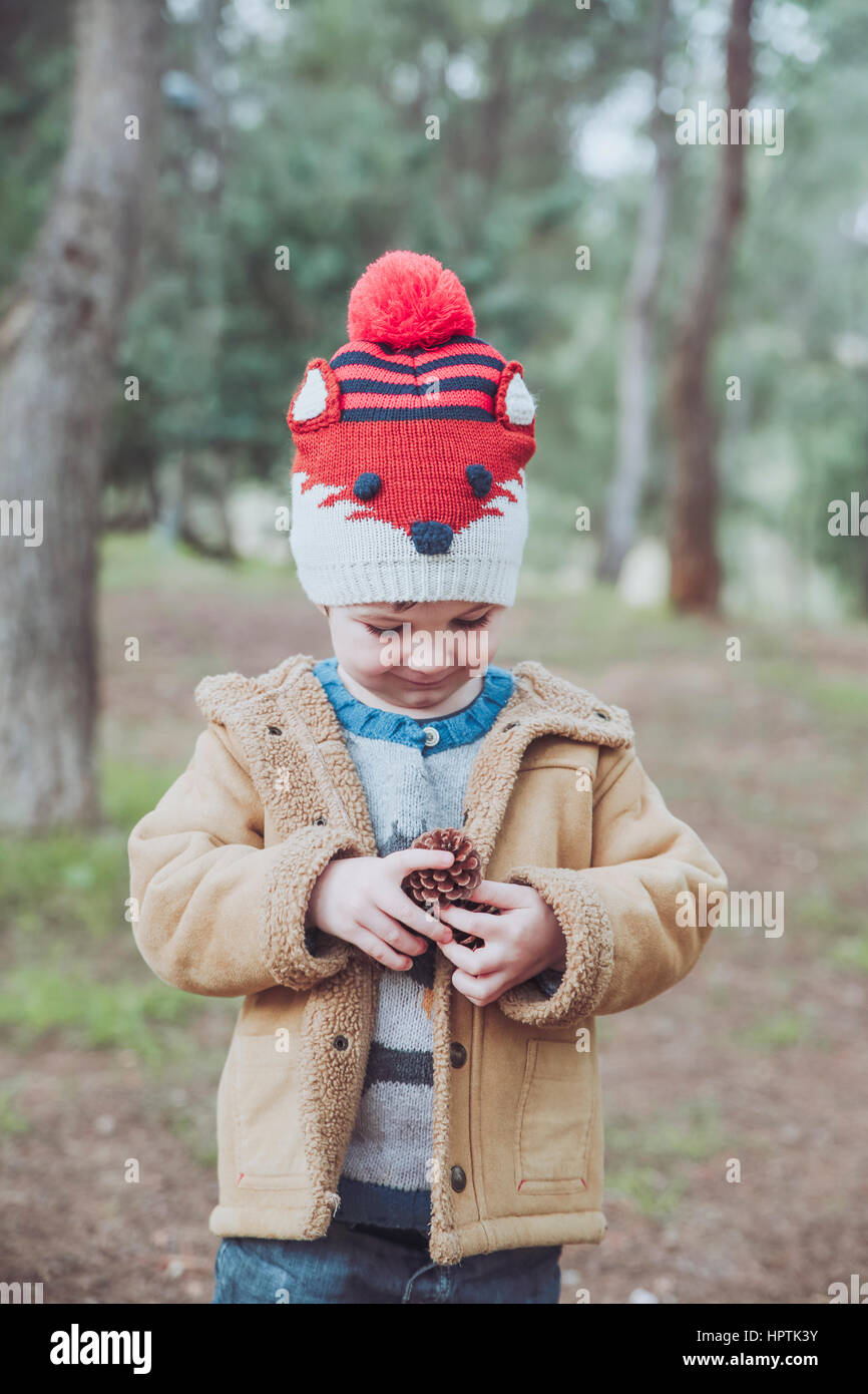 Boy wearing wooly hat holding pine cone in forest Stock Photo