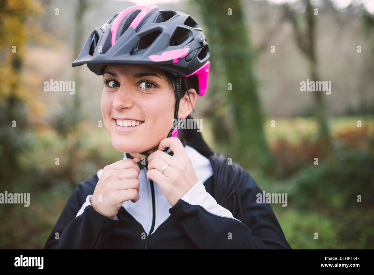Portrait of smiling woman putting on bicycle helmet Stock Photo