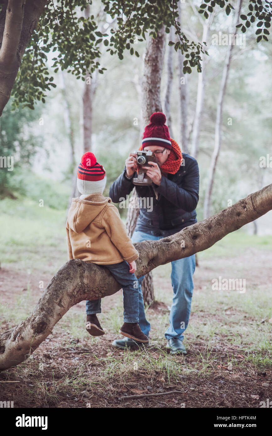 Father taking a picture of his son sitting on tree trunk in forest ...