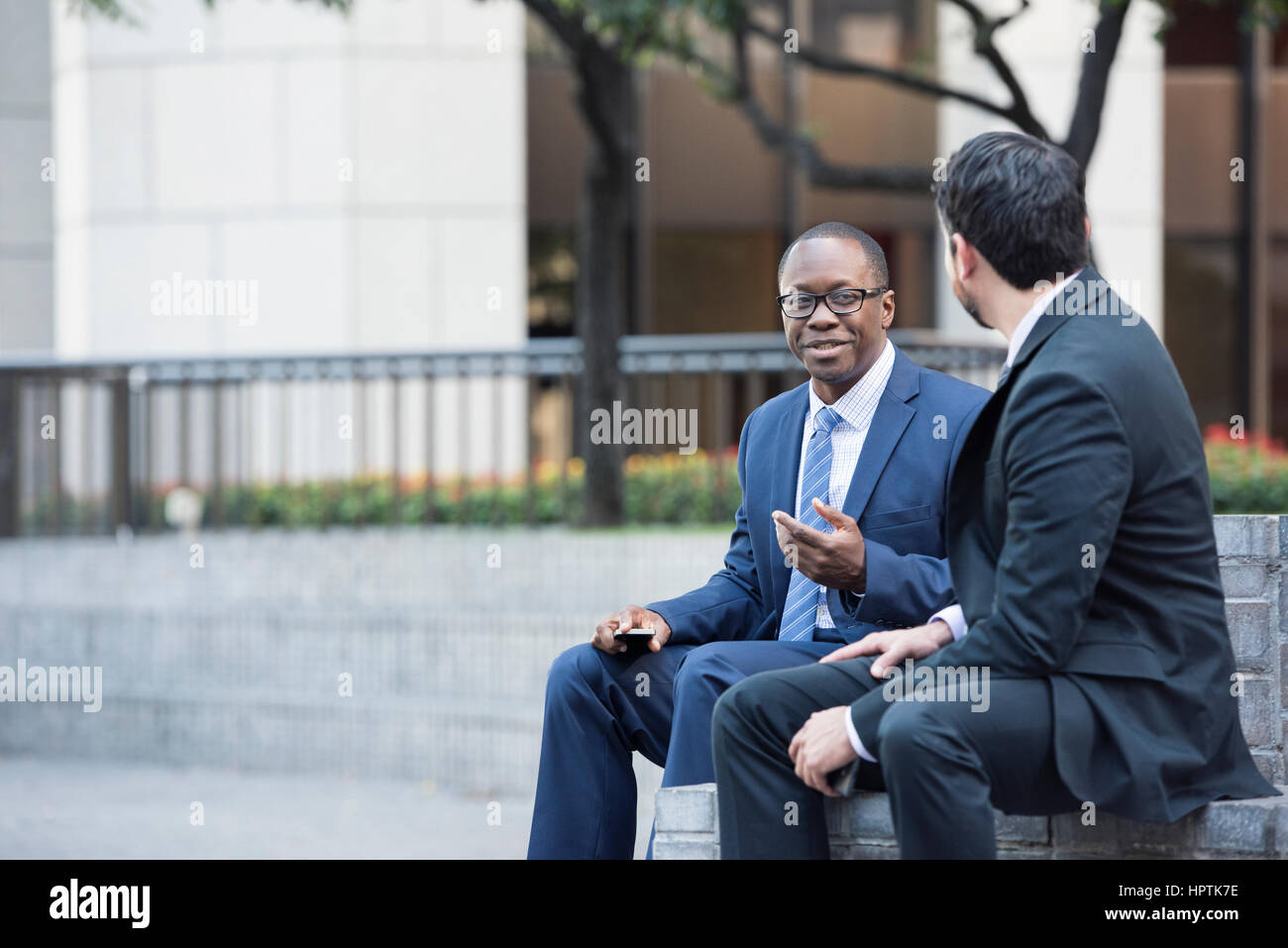 Two businessmen sitting on stairs talking Stock Photo - Alamy