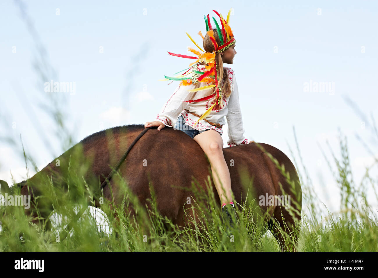 Girl wearing feather headdress riding horse on meadow Stock Photo Alamy