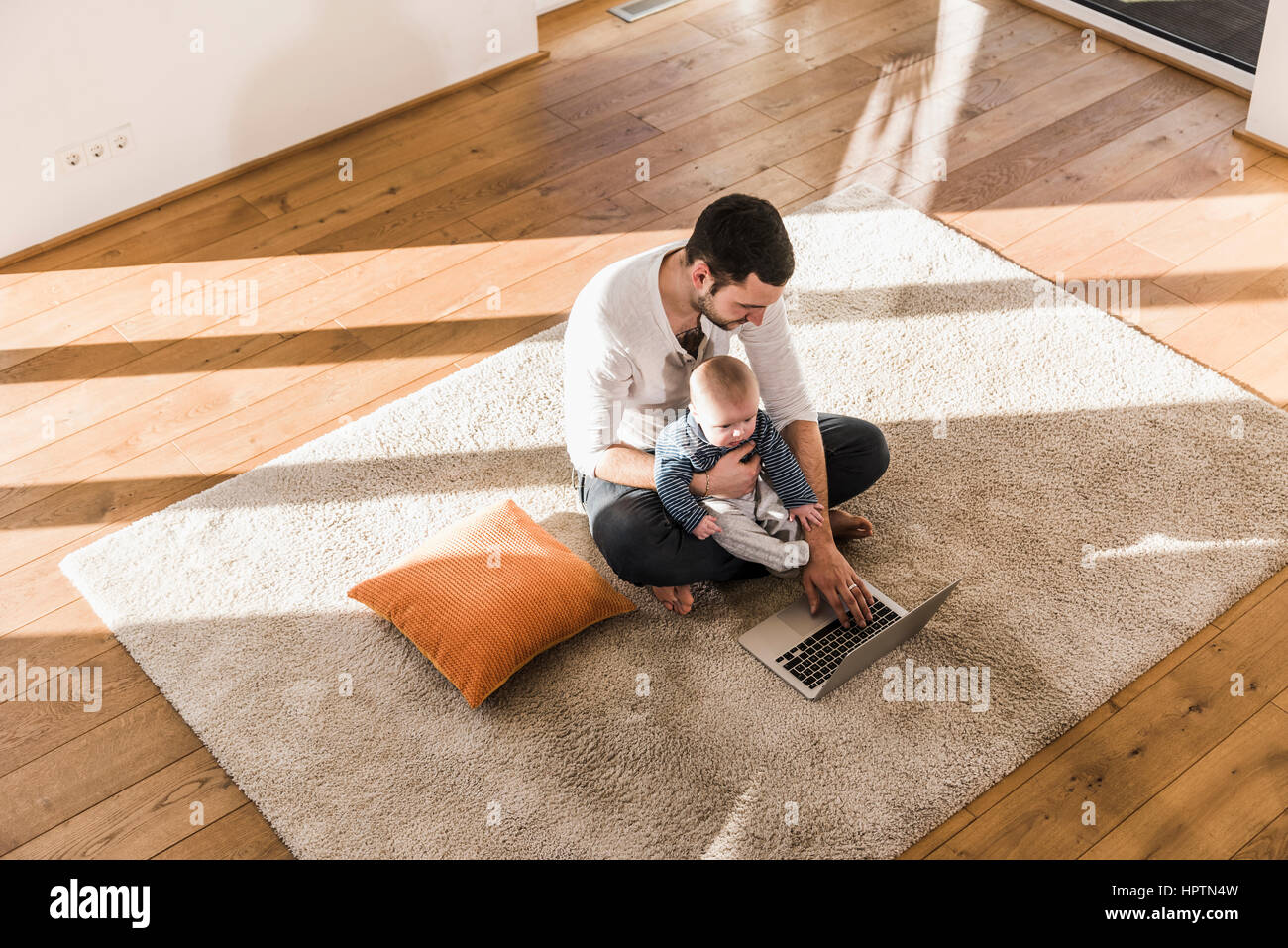Father sitting cross-legged with baby son on lap, using laptop and ...