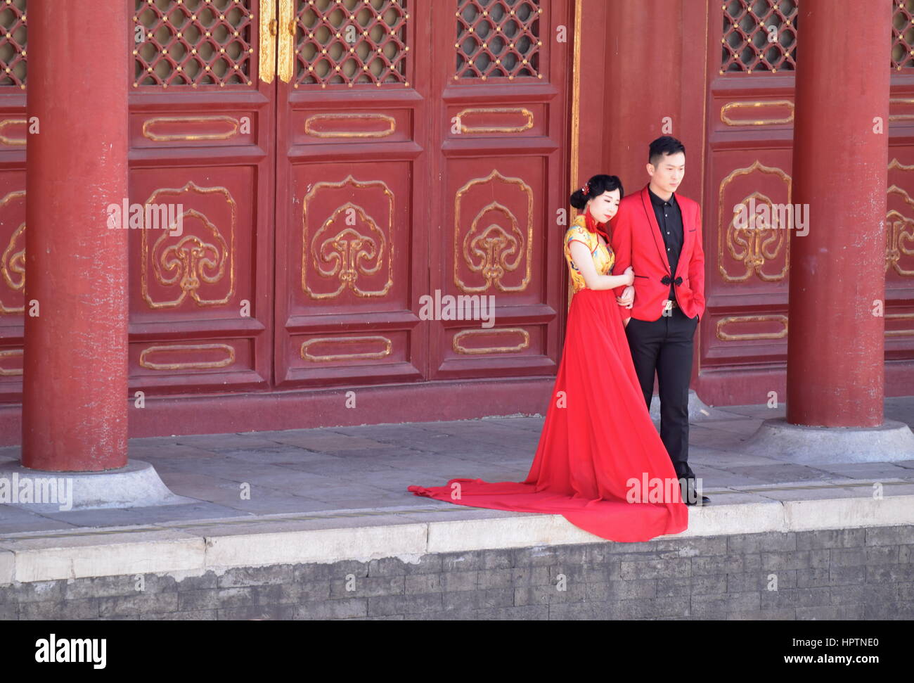 A Chinese couple in love take wedding photos at the Temple of Heaven, wearing red and surrounded by red traditional architecture - Beijing, China Stock Photo