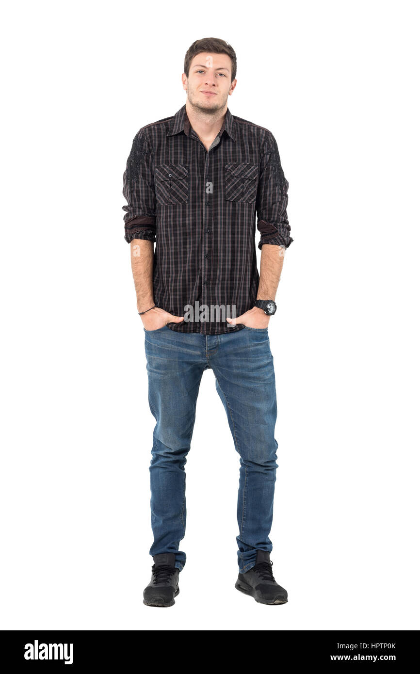 Smirking young casual man wearing jeans and plaid shirt with hands in pockets. Full body length portrait isolated over white background. Stock Photo