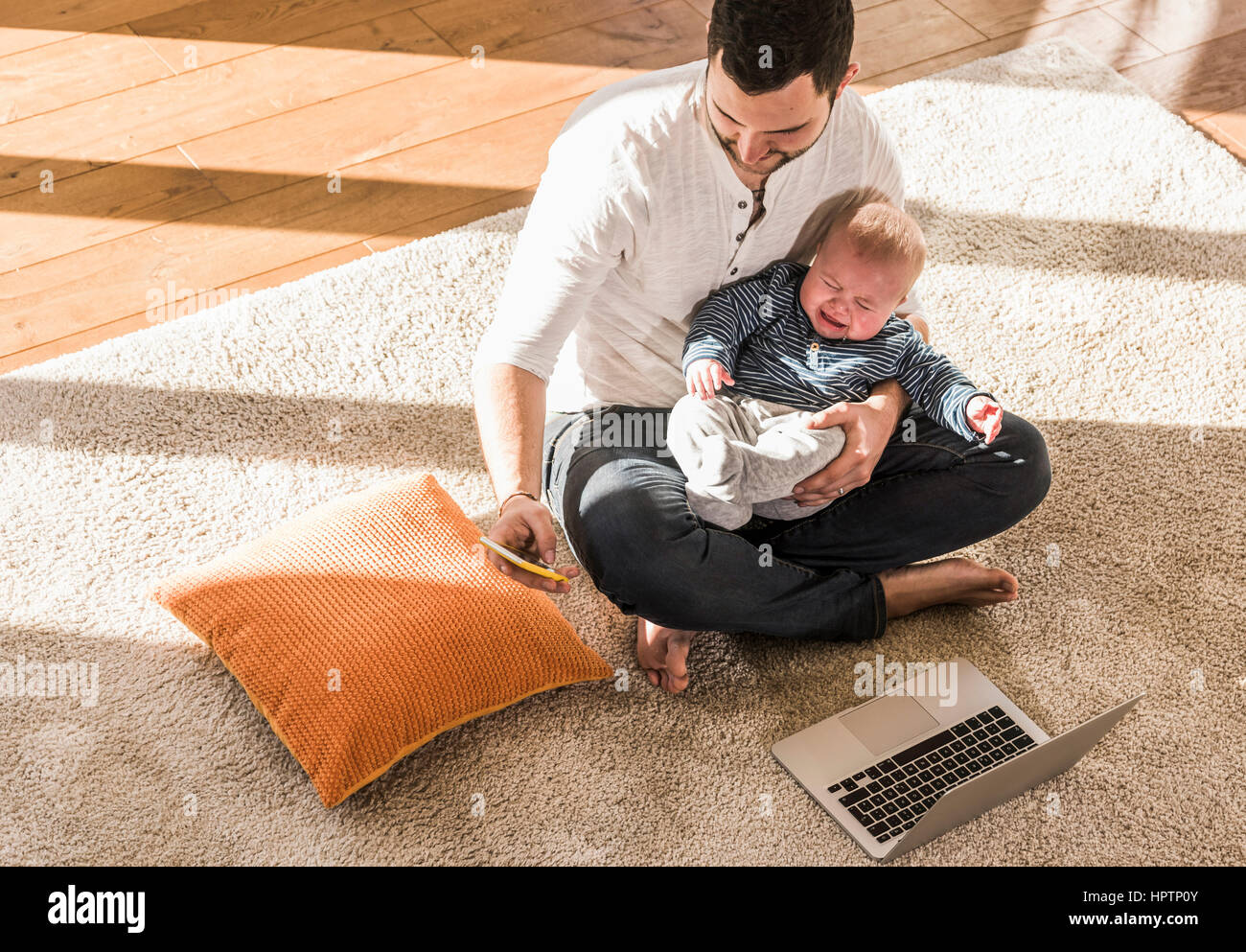 Father sitting cross-legged with baby son on lap, using laptop and ...