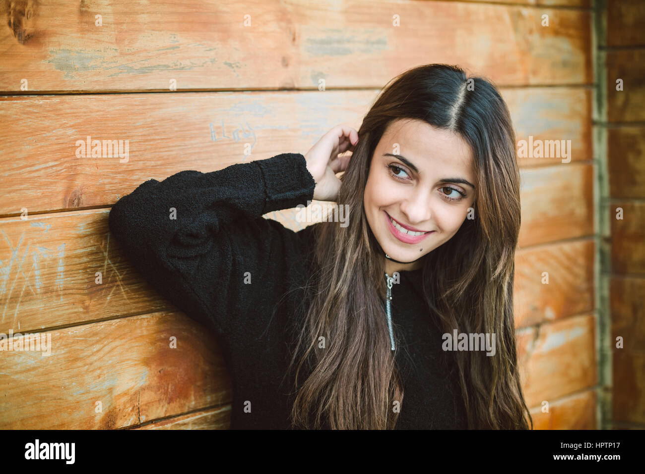 Portrait of smiling young woman in front of wooden wall watching something Stock Photo