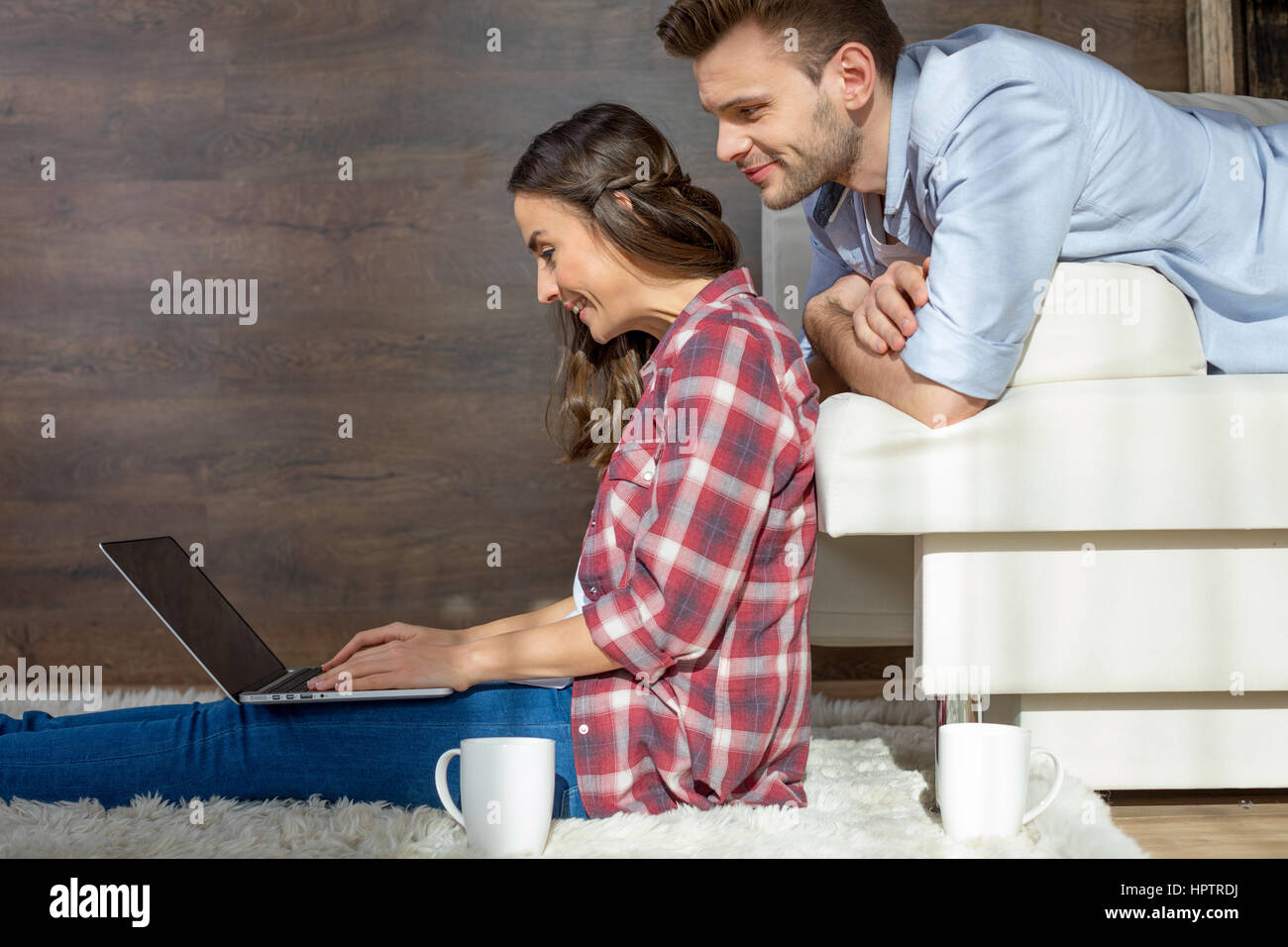 Side view of smiling young couple using laptop at home Stock Photo - Alamy