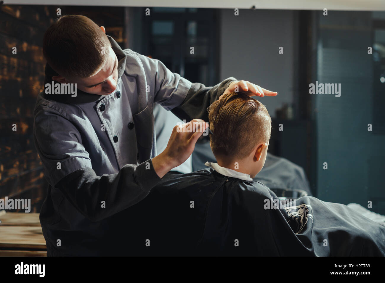 Little Boy Getting Haircut By Barber While Sitting In Chair At Barbershop. Barbershop Theme Stock Photo