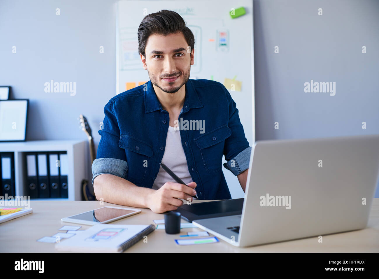 Portrait of freelance graphic designer sitting at desk with laptop and tablet Stock Photo