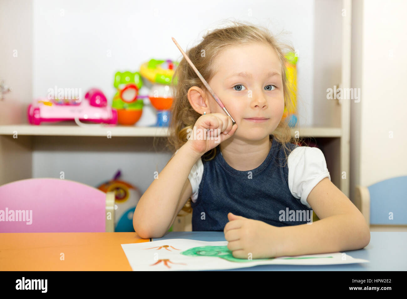 Adorable child girl draws a brush and paints in nursery room. Kid in kindergarten in Montessori preschool class. Stock Photo