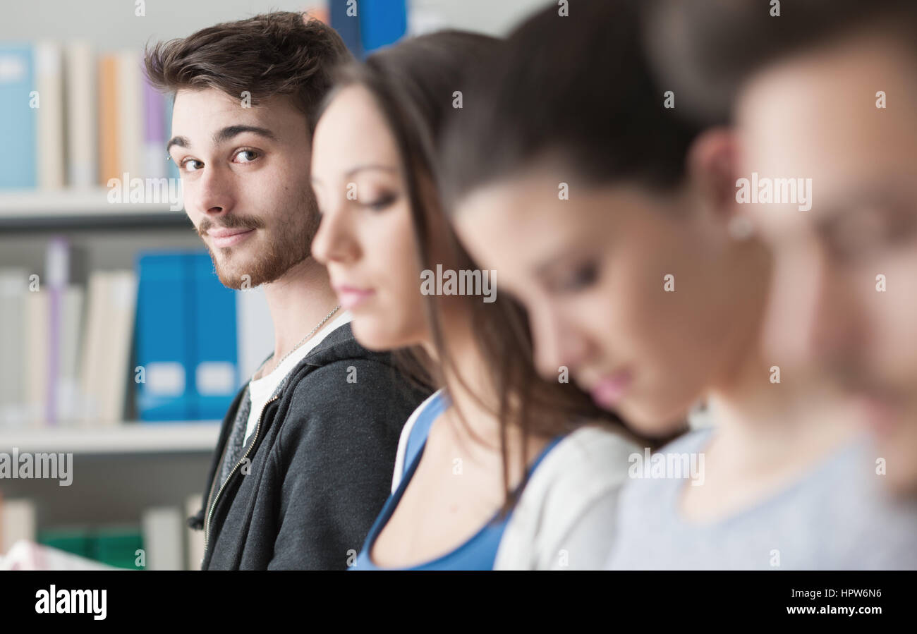 Group of college students in the library standing in line, one is smiling at camera, bookshelves on background Stock Photo