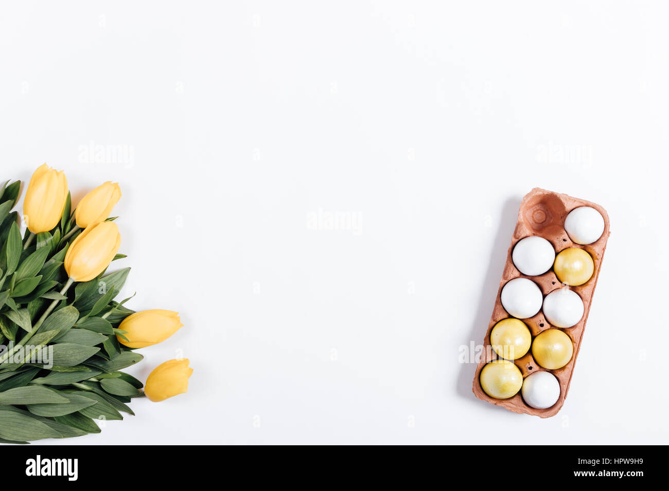 Tray with colored eggs and yellow tulips on a white table top view ...