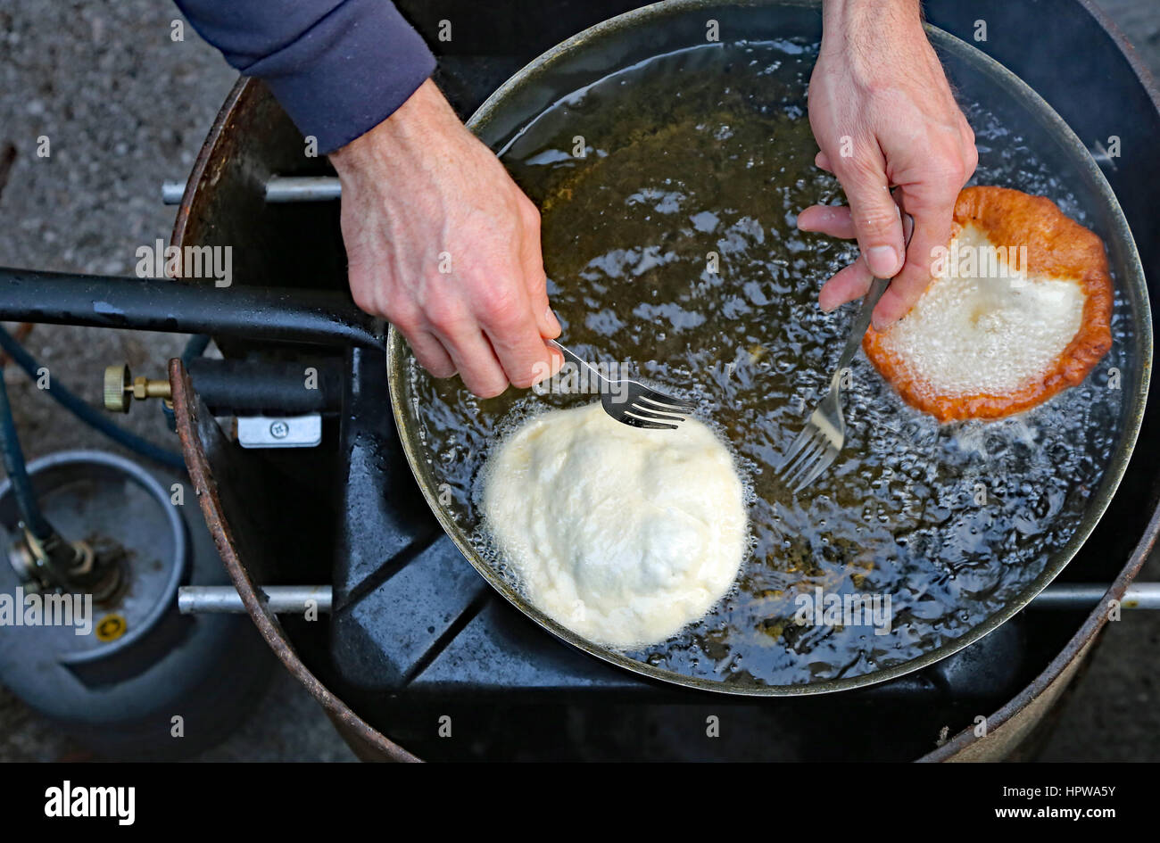 Cook hands two pancakes in a frying pan with hot oil in a street food