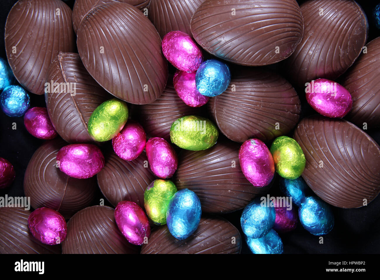 Pile of foil wrapped & unwrapped chocolate easter eggs in pink, blue & lime green. Stock Photo