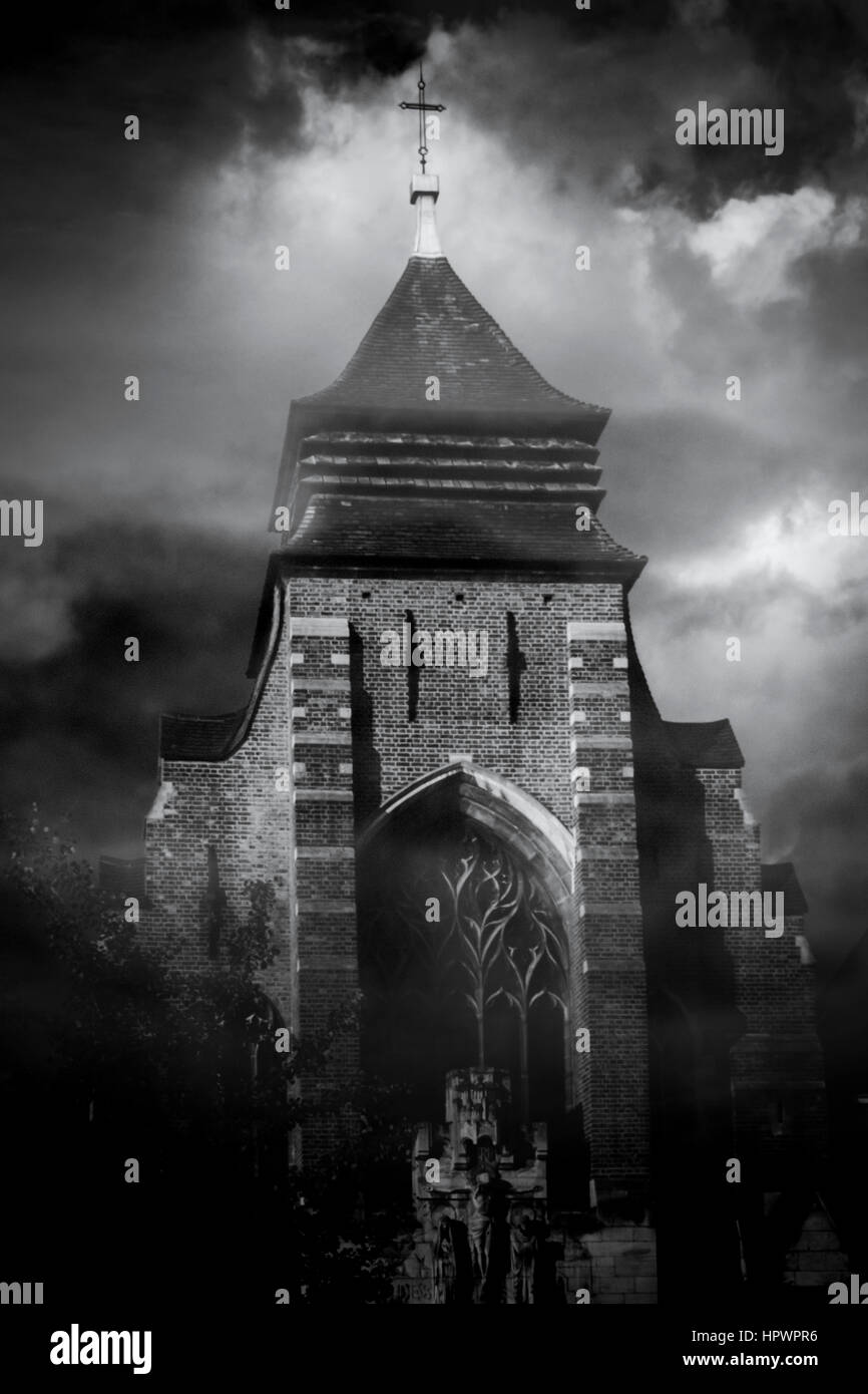Black and white image of a church tower looming from the mist against a cloudy moonlit night sky Stock Photo