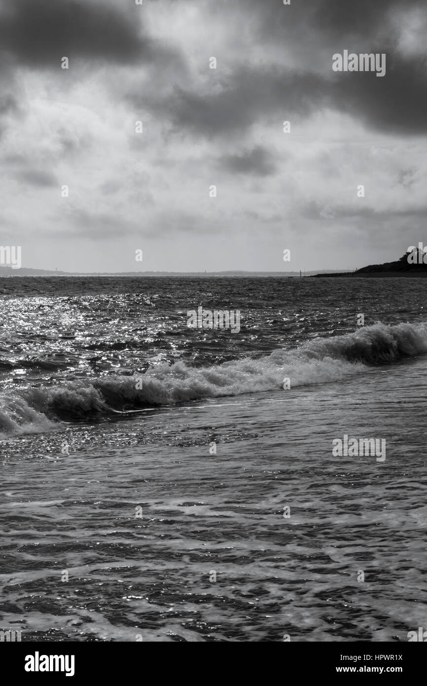 Black and white photo of a stormy sky over waves breaking on a shingle ...