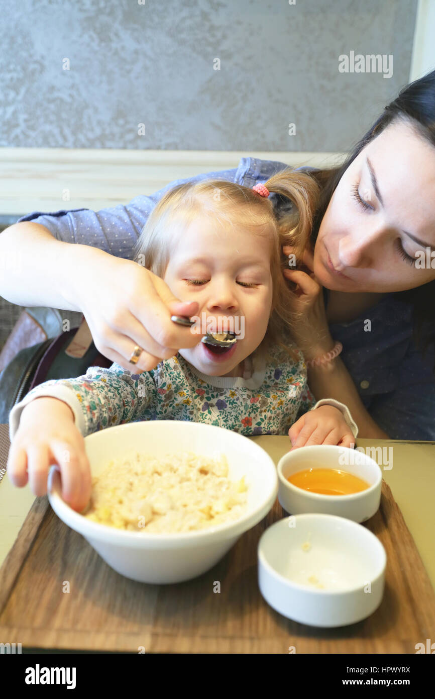 Mother feeding porridge her kid with healthy breakfast Stock Photo