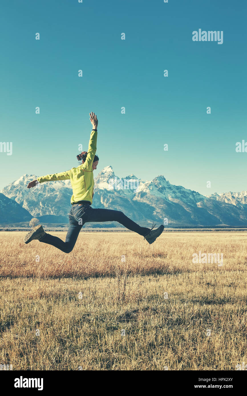 Retro stylized picture of a happy young woman jumping on a mountain meadow, Grand Teton National Park, Wyoming, USA. Stock Photo