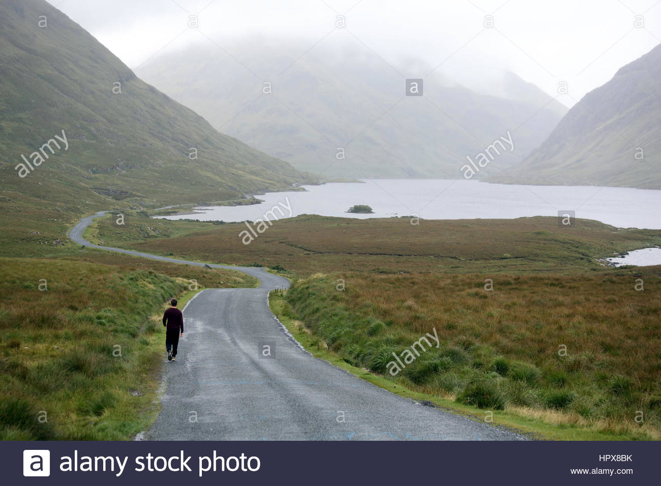 A young man walks the road through Doolough Valley in Mayo Ireland on his journey through the west. Stock Photo