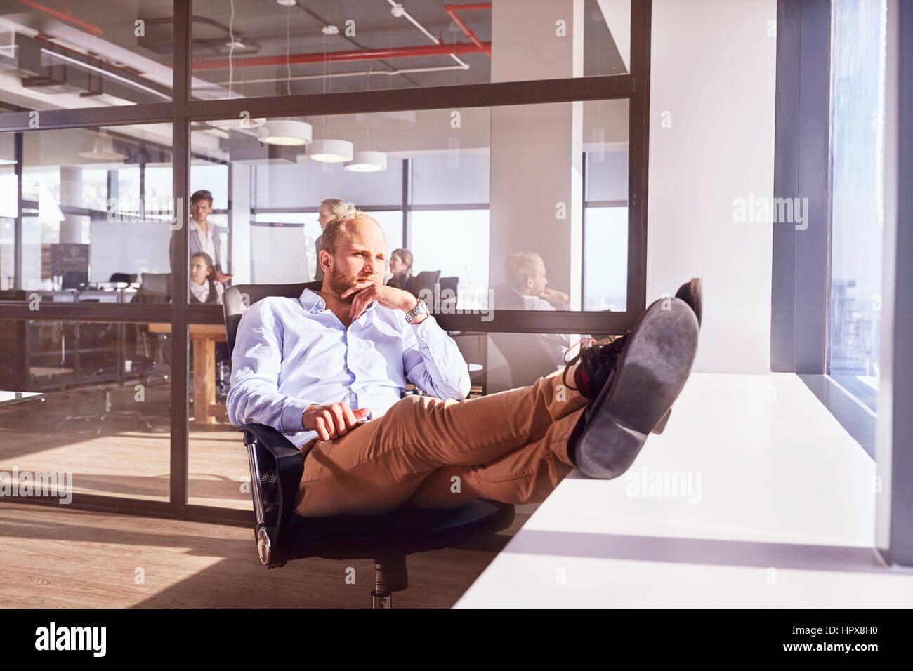 Pensive businessman sitting with feet up looking through sunny window in office Stock Photo