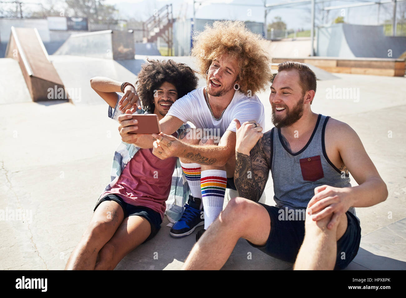Male friends with camera phone taking selfie at sunny skate park Stock Photo