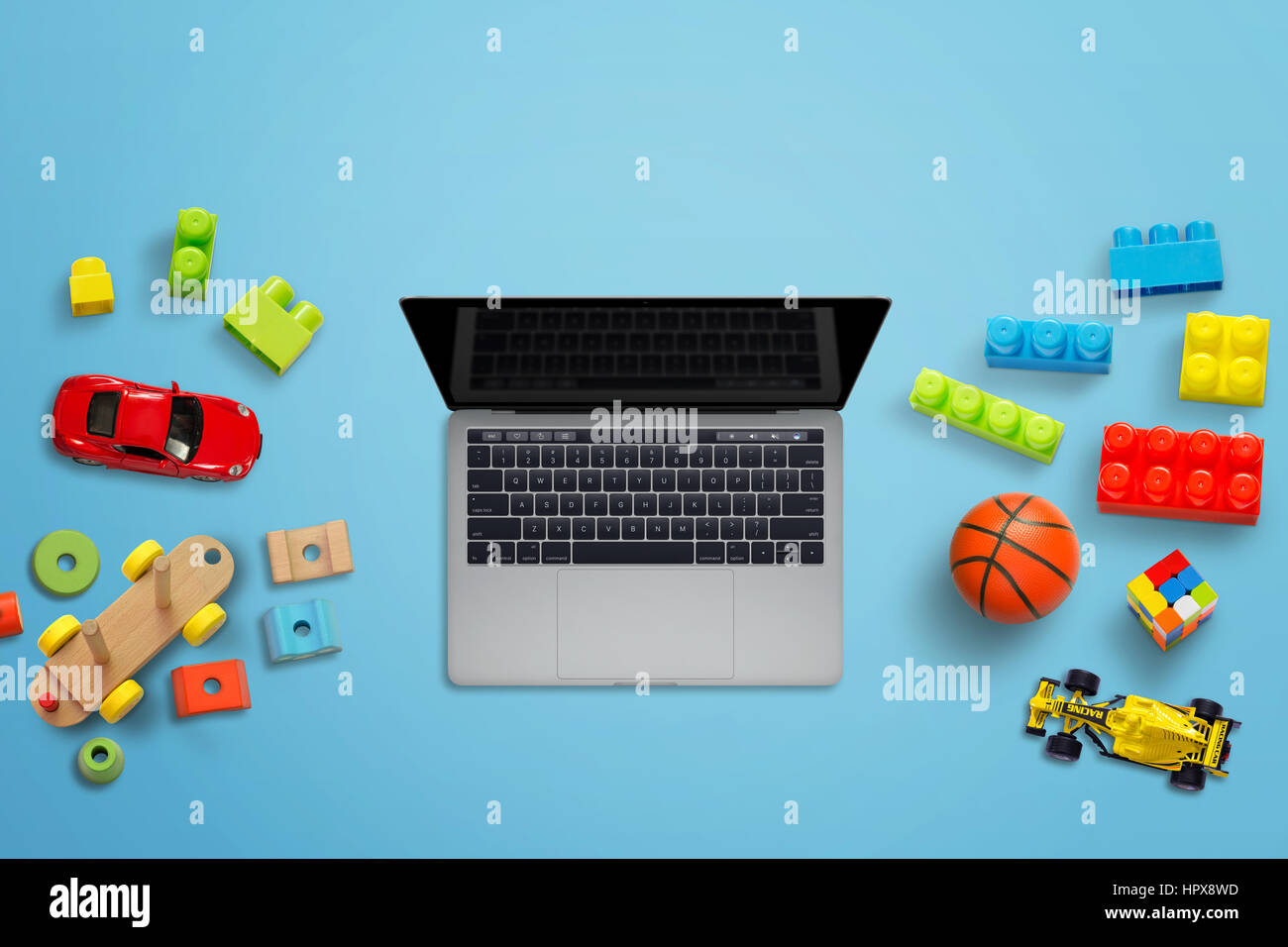Laptop computer and kid toys on blue desk. Top view. Blank display for app, game mockup presentation. Stock Photo