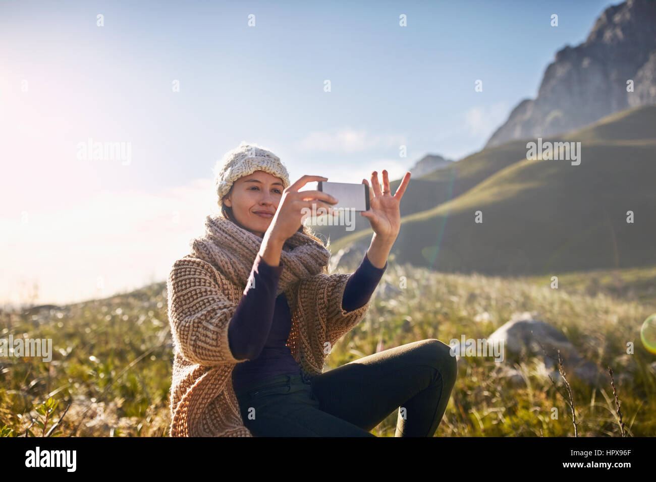 Young woman using camera phone in sunny, remote valley Stock Photo