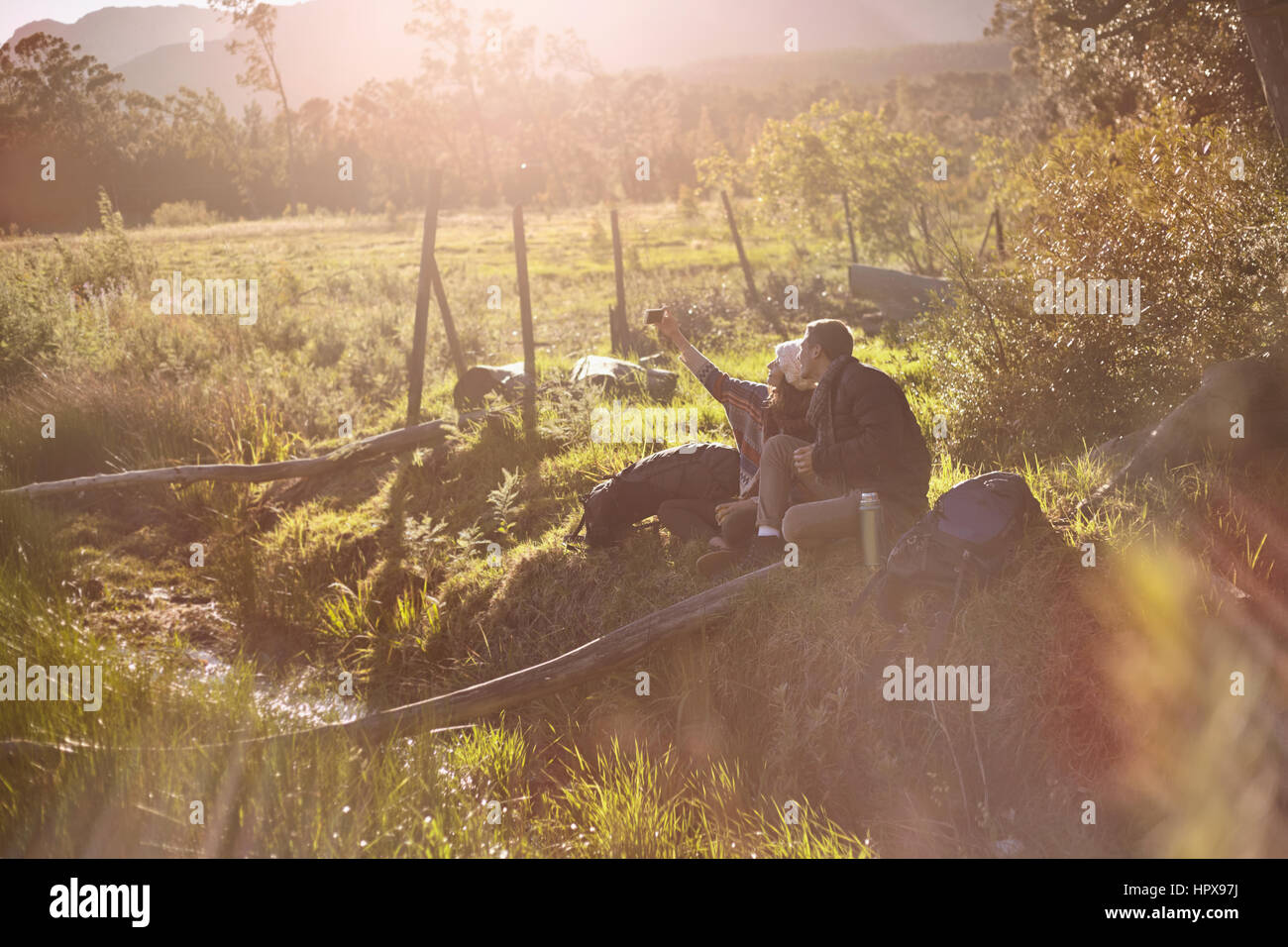 Young couple with camera phone taking selfie in sunny, remote field Stock Photo