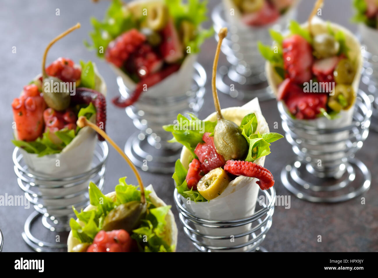 Mini tortillas stuffed with octopus salad with olives and capers, served in wire egg cups Stock