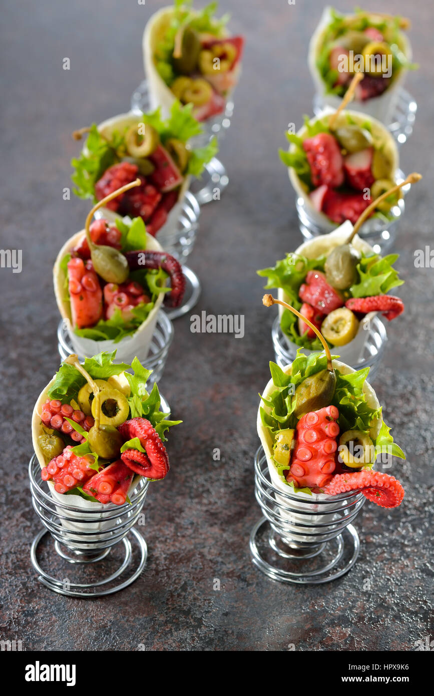 Mini tortillas stuffed with octopus salad with olives and capers, served in wire egg cups Stock Photo