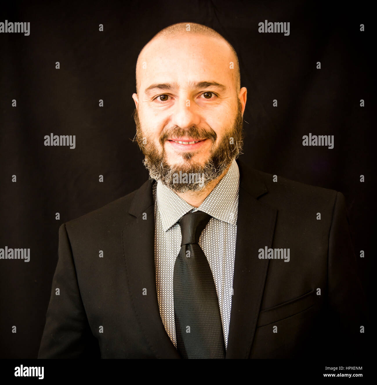Handsome, bald man with beard, in suit and tie, on black background ...
