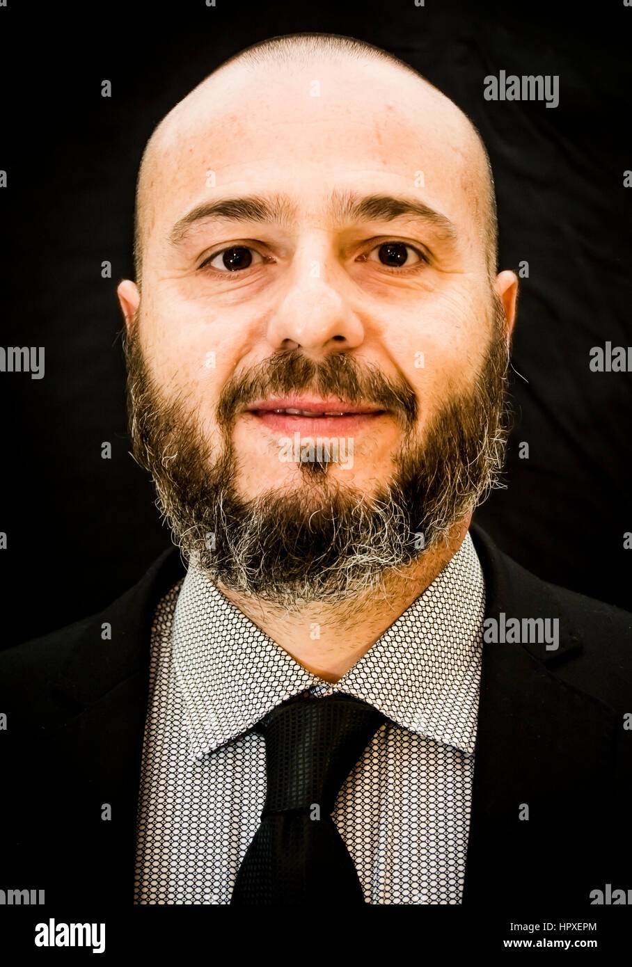 Handsome, bald man with beard, in suit and tie, on black background ...