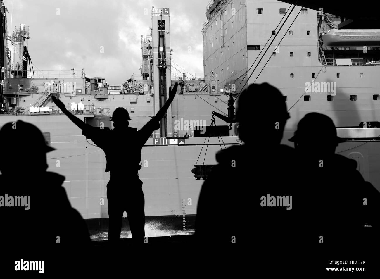 Boatswain's Mate 1st Class Stephen Markman, assigned to the aircraft carrier USS George H W Bush signals to personnel abroad the Military Sealift Command dry cargo and ammunition ship USNS William McLean during an ammunition onload, January 15, 2013. Image courtesy US Navy Mass Communication Specialist 3rd Class Timothy Daughton. Stock Photo