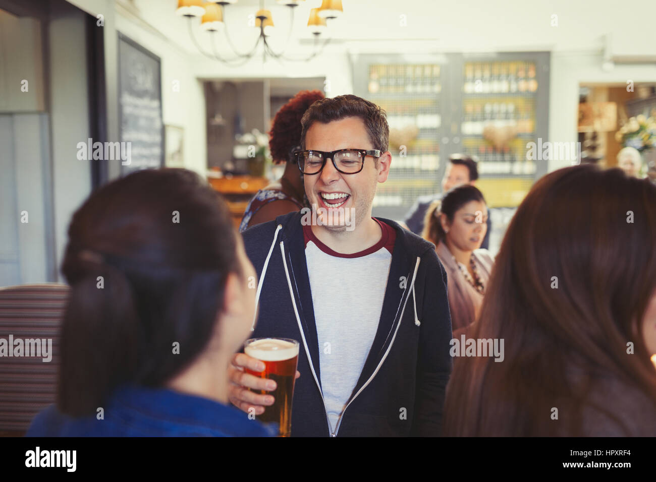 Man laughing and drinking beer with friends at bar Stock Photo