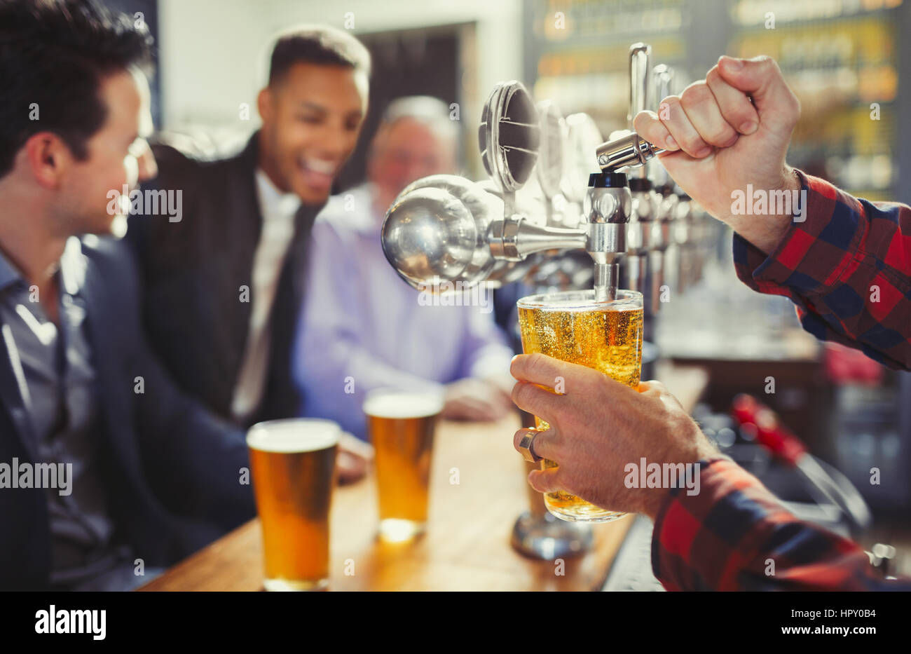 Bartender pouring beer from tap behind bar Stock Photo
