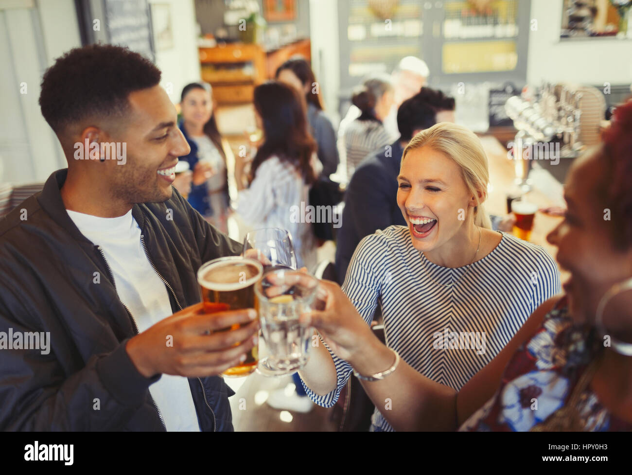 Laughing friends toasting beer and wine glasses at bar Stock Photo