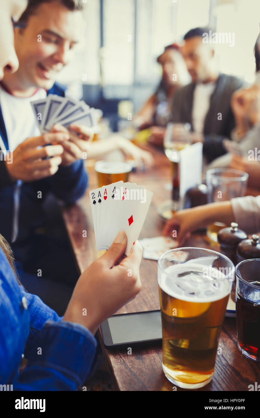 Woman holding aces four of a kind playing poker and drinking beer with friends at bar Stock Photo