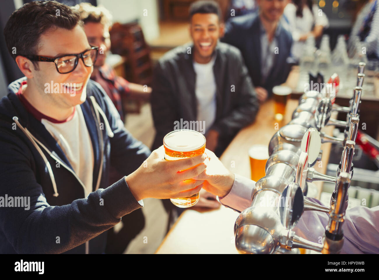 Smiling man receiving beer from bartender at bar Stock Photo