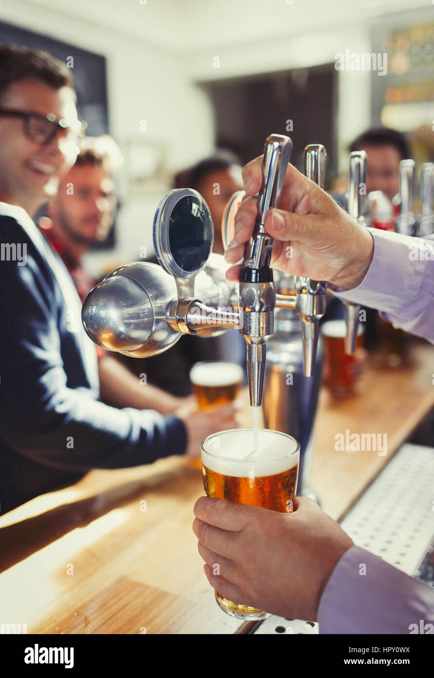 Close up bartender pouring beer from tap handle behind bar Stock Photo