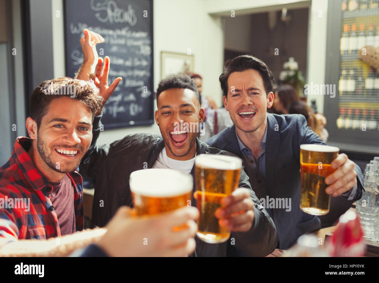 Portrait enthusiastic men friends toasting beer glasses at bar Stock Photo