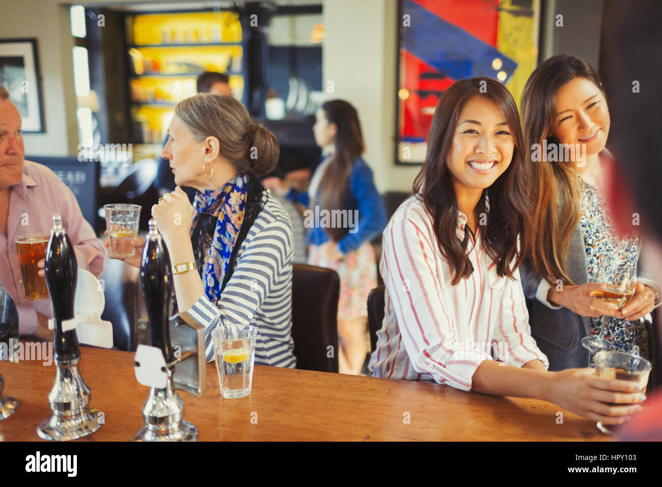 Women smiling at bartender and drinking at bar Stock Photo